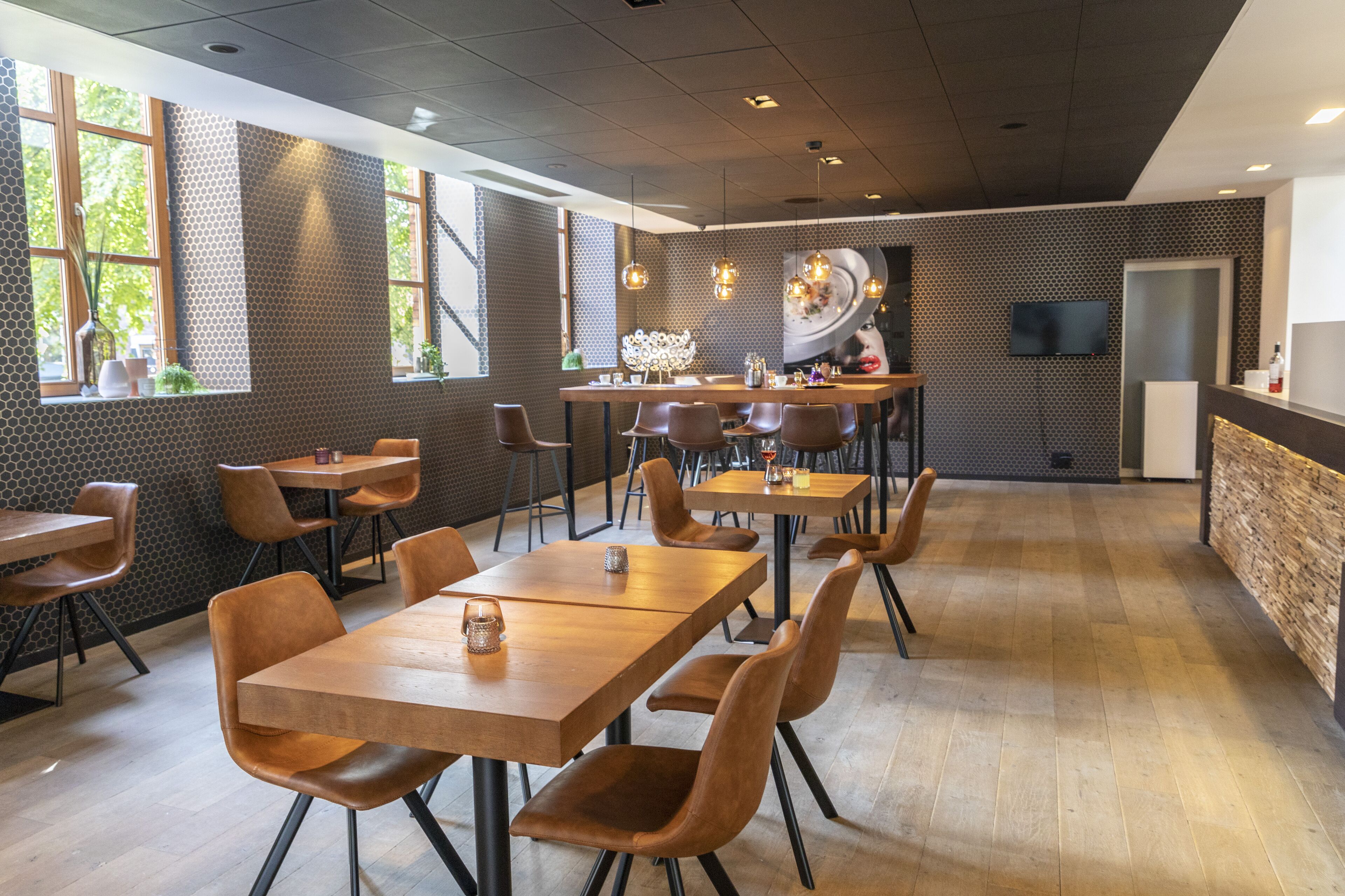 A modern restaurant with wooden tables and chairs, a large window with plants, and a flat-screen TV on the wall.