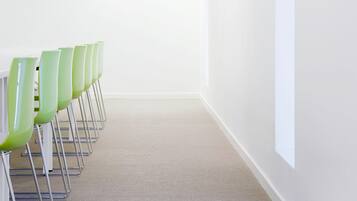 Uma sala de conferências com uma mesa comprida e cadeiras verdes, paredes brancas e chão coberto de carpete.