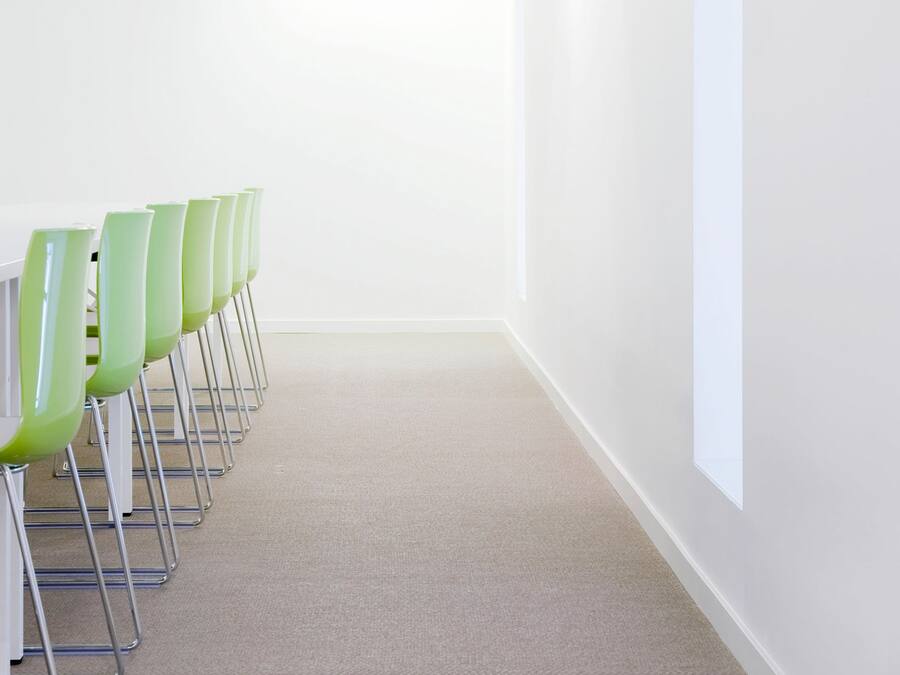 Uma sala de conferências com uma mesa comprida e cadeiras verdes, paredes brancas e chão coberto de carpete.