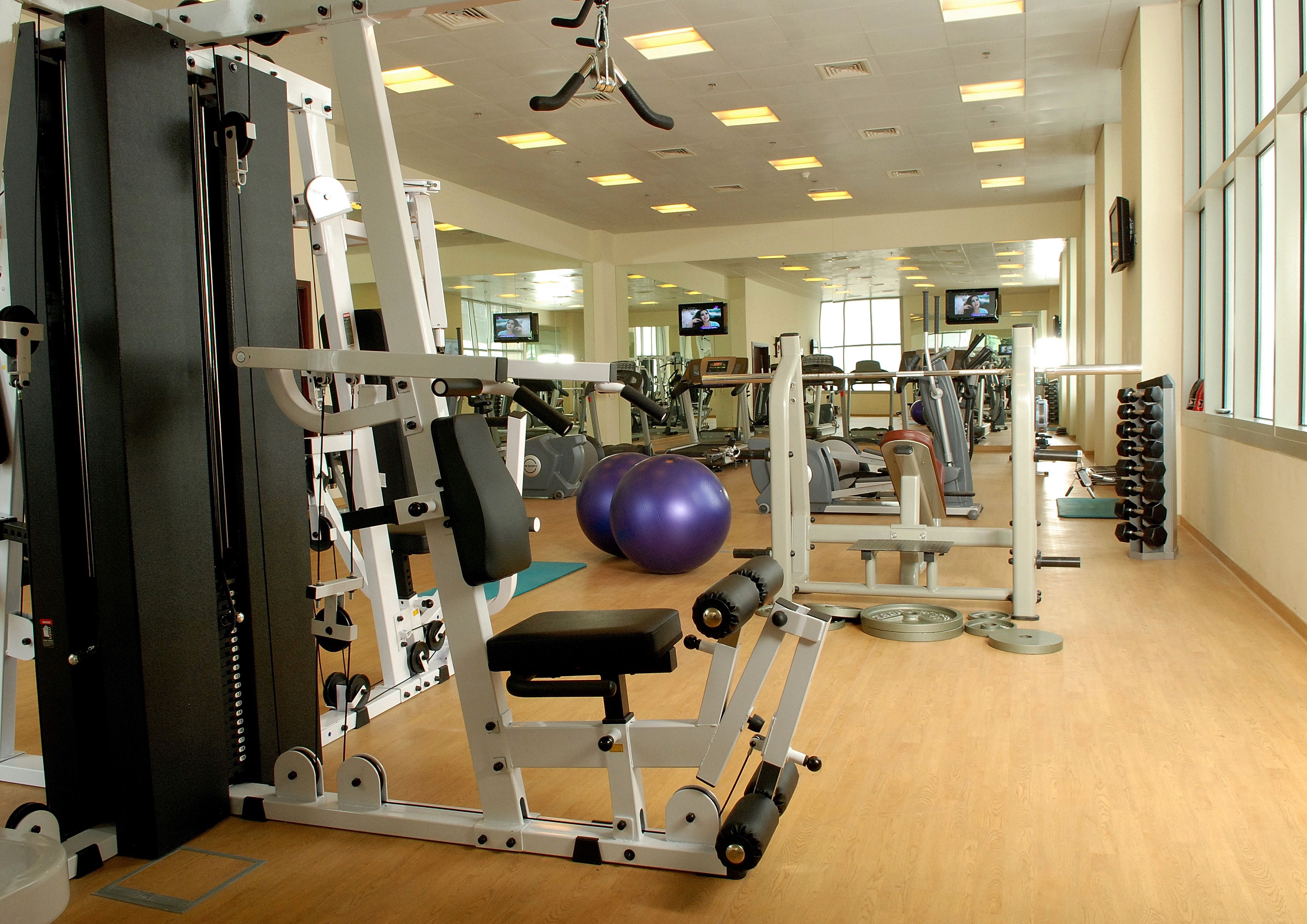 Una palestra con diverse attrezzature per esercizi, un grande specchio e numerosi schermi televisivi.