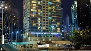 A high-rise building with illuminated windows and balconies, surrounded by other tall buildings. - Oaks Liwa Heights Suites (Dubai)