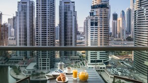 A balcony with a breakfast setup including croissants, coffee, and orange juice, overlooking a cityscape with tall buildings. - Oaks Liwa Heights Suites (Dubai)