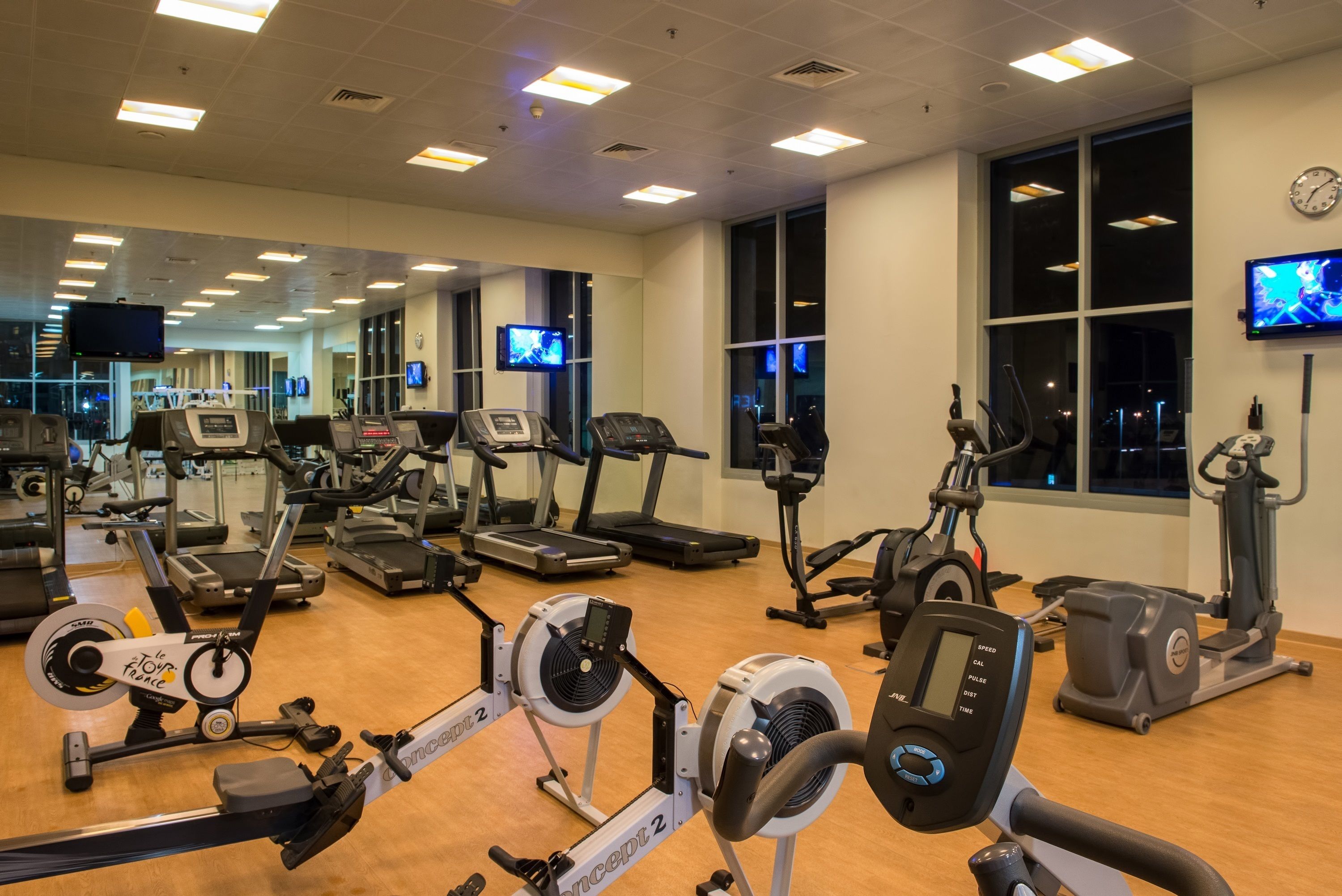 Ett gym med olika typer av konditionsmaskiner, speglar och flera tv-skärmar.