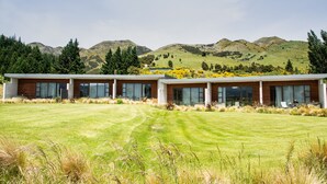 A modern two-story building with large windows and a flat roof, situated in a grassy field with mountains in the background. - Braemar Lodge And Spa (Hanmer Springs)