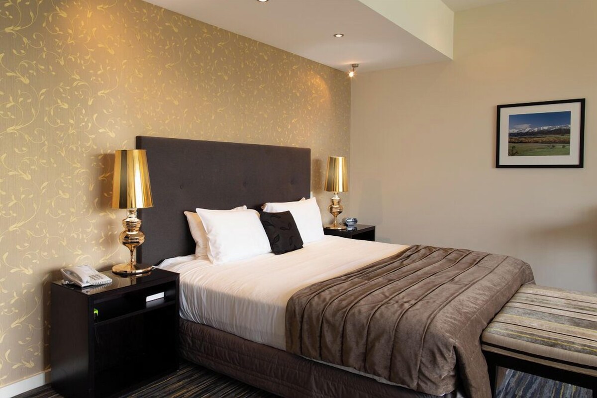 A hotel room with a large bed, two bedside tables with lamps, a telephone, and a framed picture on the wall.
