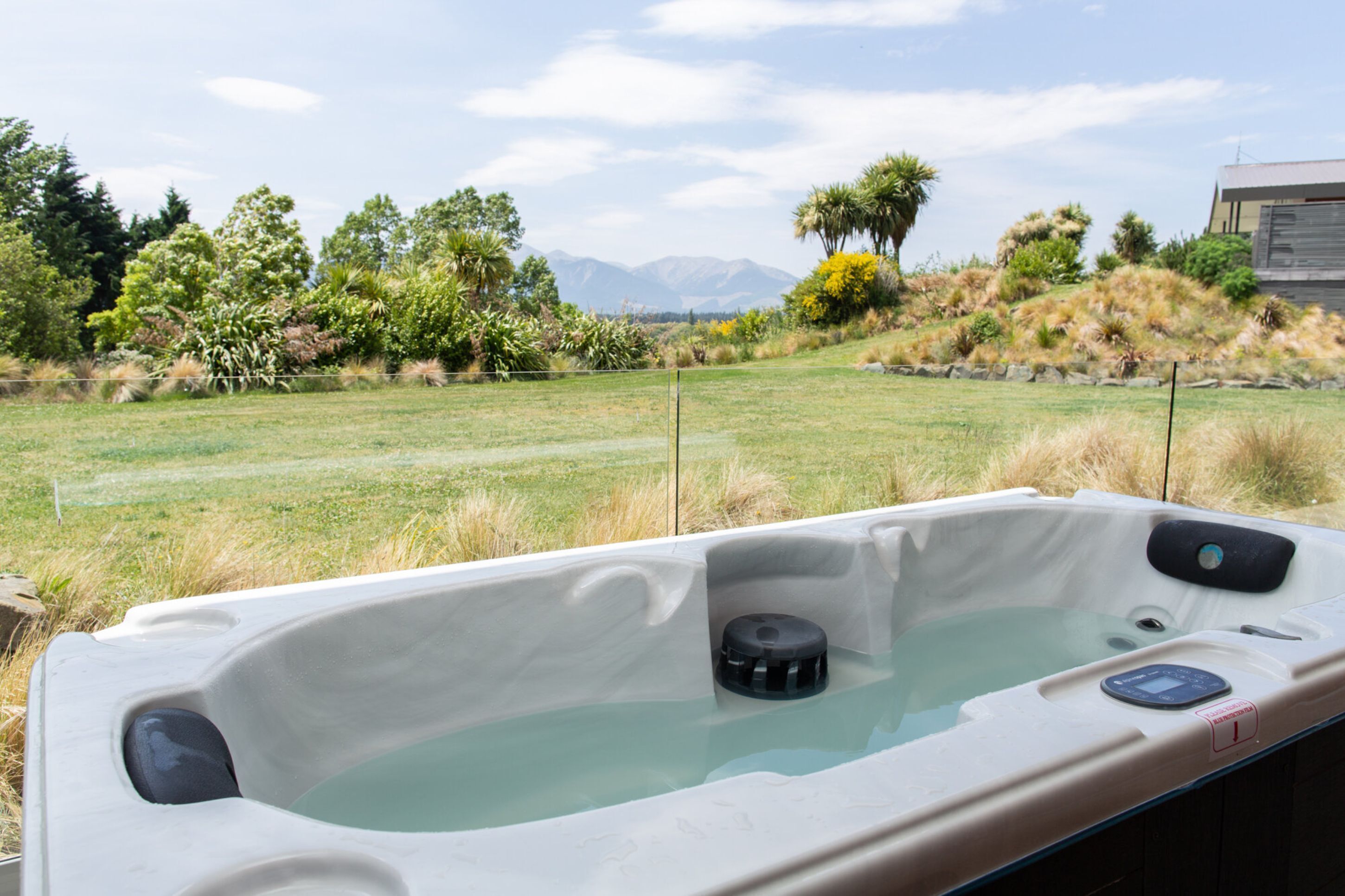 Un jacuzzi con panel de control, rodeado de césped, árboles y una montaña al fondo.