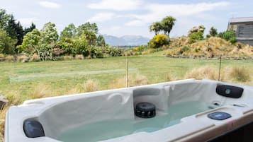 Un jacuzzi con panel de control, rodeado de césped, árboles y una montaña al fondo.