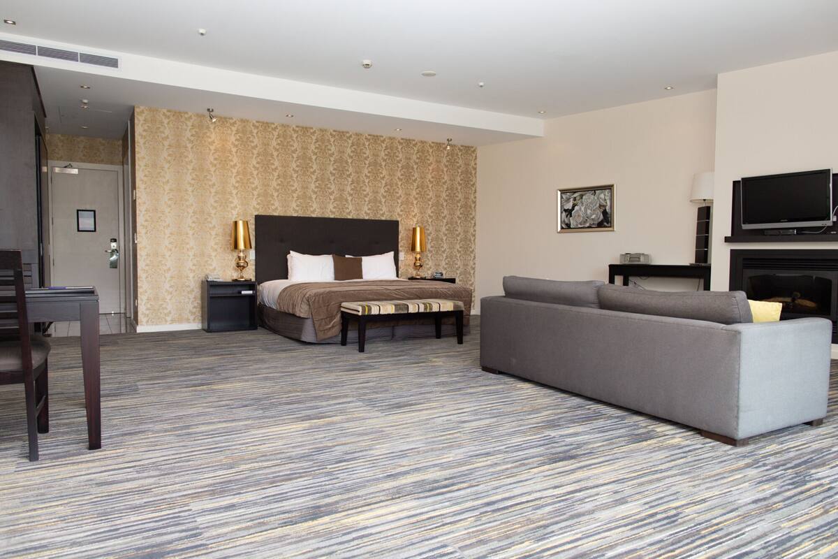 A hotel room with a bed, a sofa, a TV, and a fireplace.