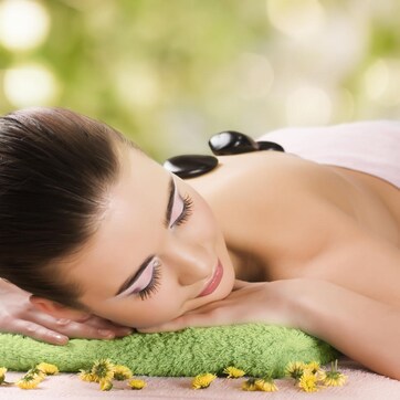 A person lying on a green towel with yellow flowers, suggesting a spa setting.