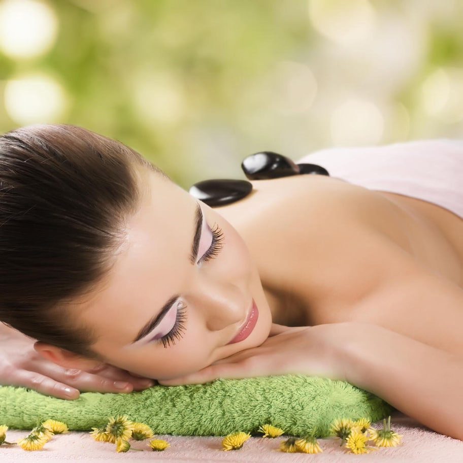 A person lying on a green towel with yellow flowers, suggesting a spa setting.