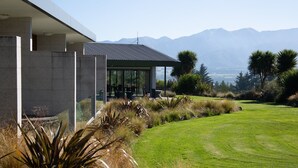 A modern house with a patio, surrounded by a well-maintained lawn and mountains in the background. - Braemar Lodge And Spa (Hanmer Springs)