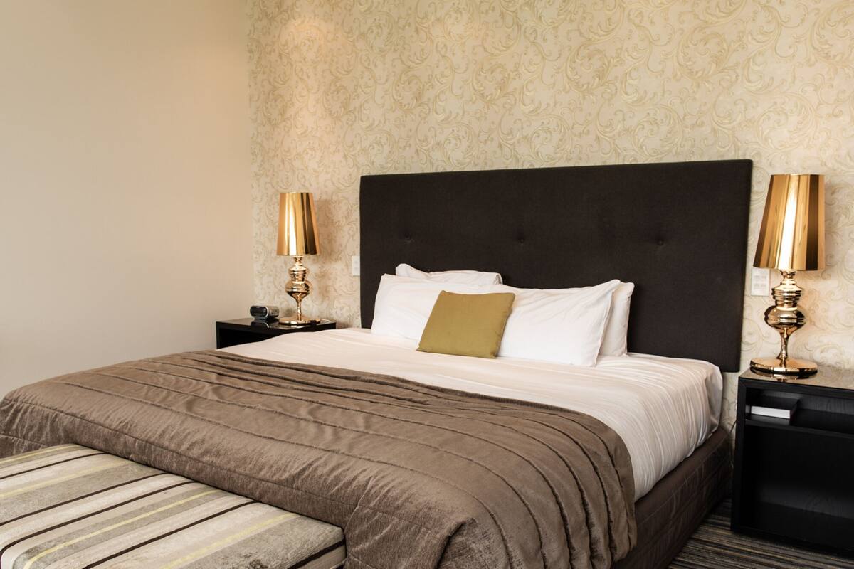 A neatly made bed with a dark headboard, two bedside tables with lamps, and a patterned wallpaper.