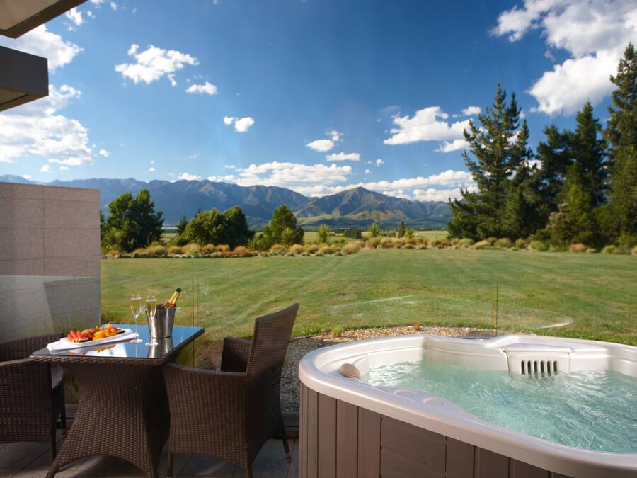 Un jacuzzi con vista a la montaña, una mesa con una botella de champán y sillas de mimbre.