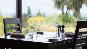 A table set for two with wine glasses and a salt and pepper shaker, overlooking a scenic view with palm trees and yellow flowers. - Braemar Lodge And Spa (Hanmer Springs)