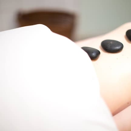 A massage therapy session with a person lying down and several black stones placed on their back.