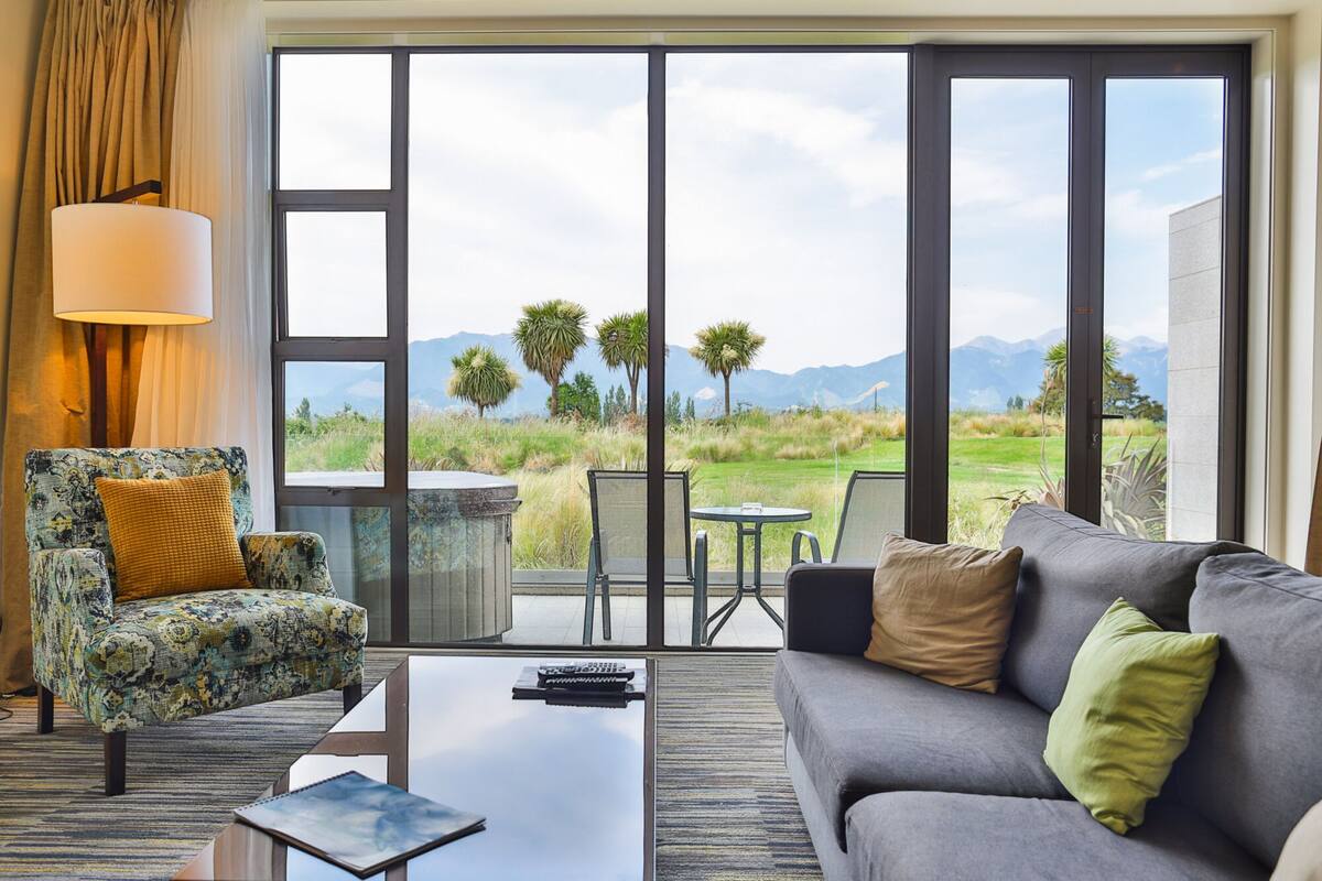 A room with a sofa, armchair, and a table with a lamp.