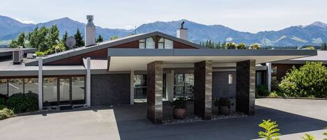 A modern house with a covered patio, large windows, and a mountain backdrop.