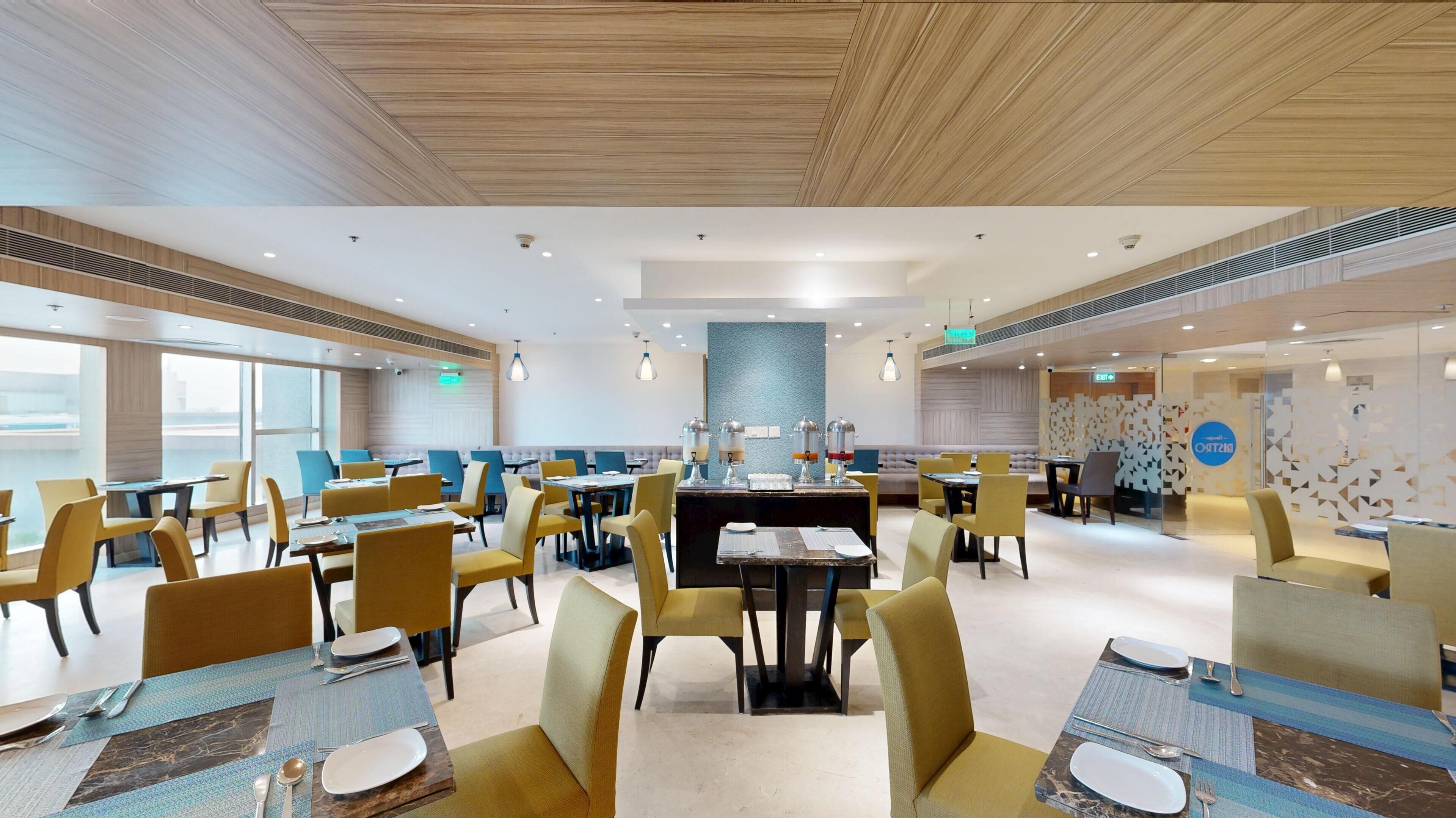 A spacious dining area with multiple tables and chairs, a central buffet station, and a modern ceiling design.
