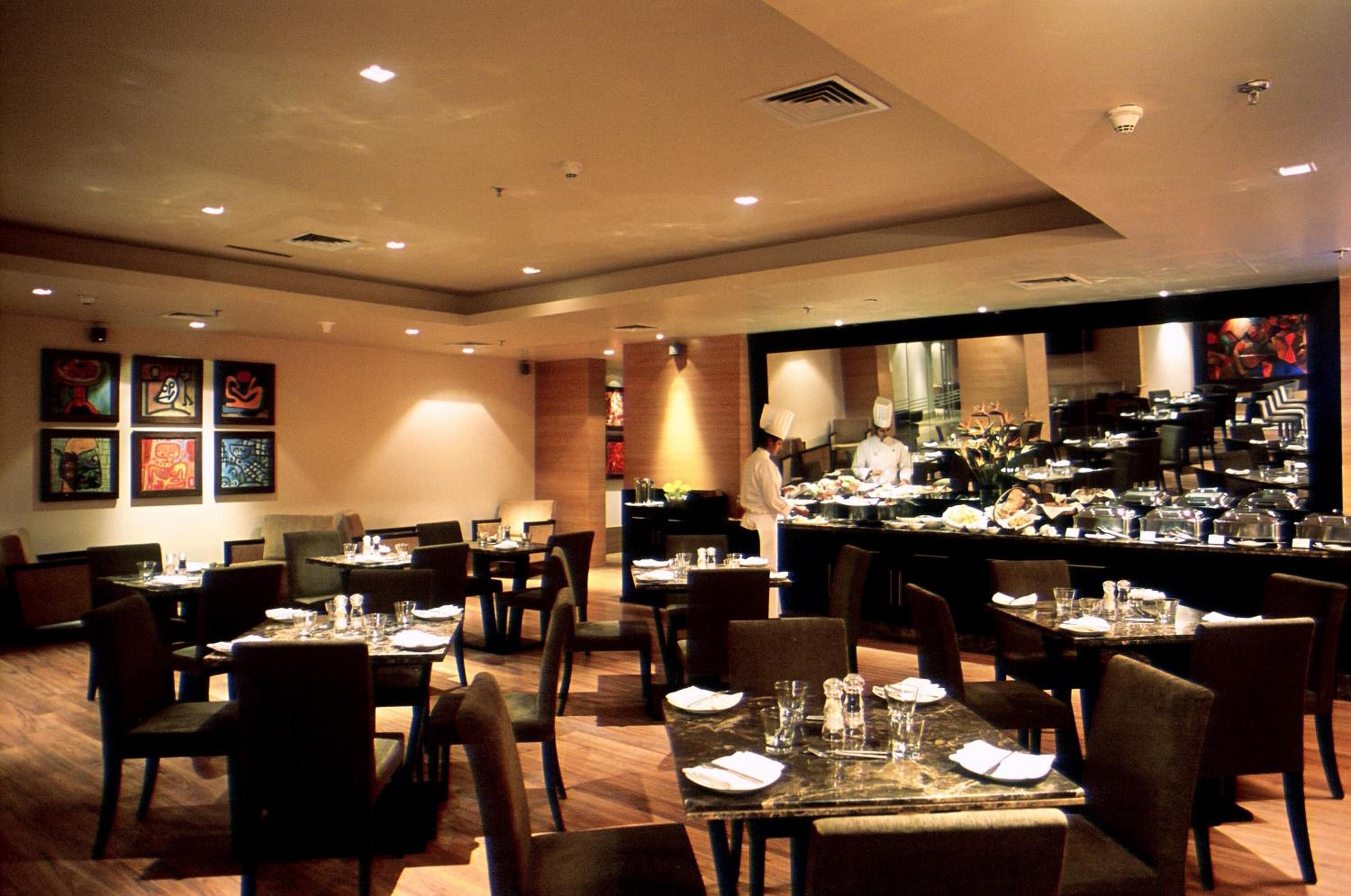 A restaurant with multiple dining tables and chairs, a kitchen area, and artwork on the walls.