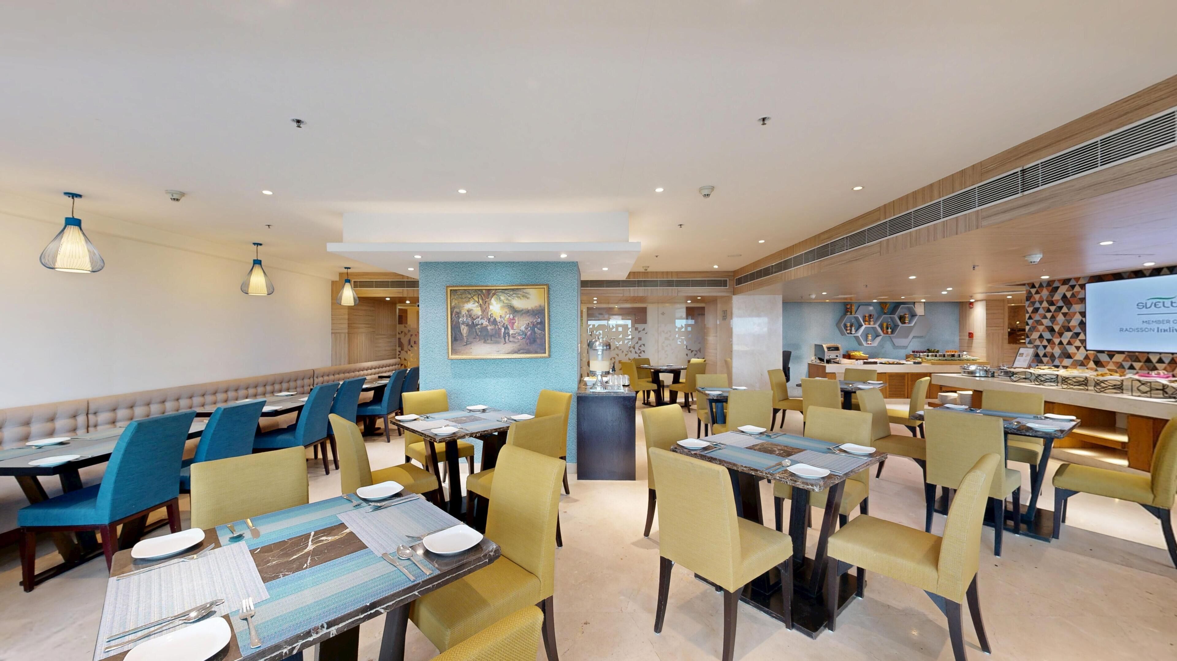 A restaurant with multiple dining tables and chairs, a bar area, and a wall-mounted painting.