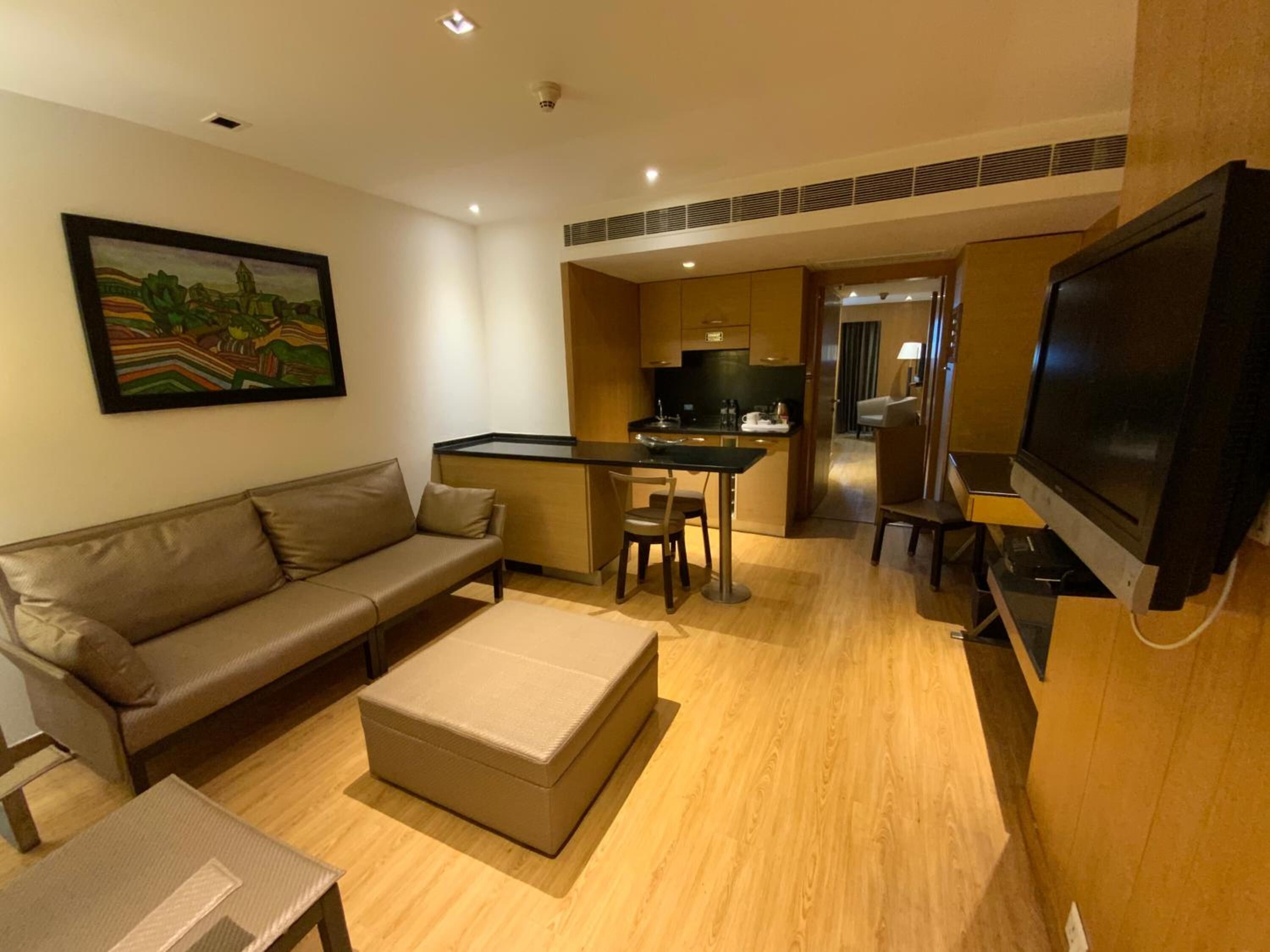 A modern living room with a sofa, ottoman, TV, and a small dining area with a table and chairs.