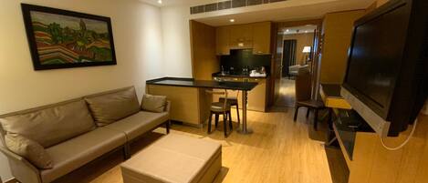 A modern living room with a sofa, ottoman, TV, and a small dining area with a table and chairs.