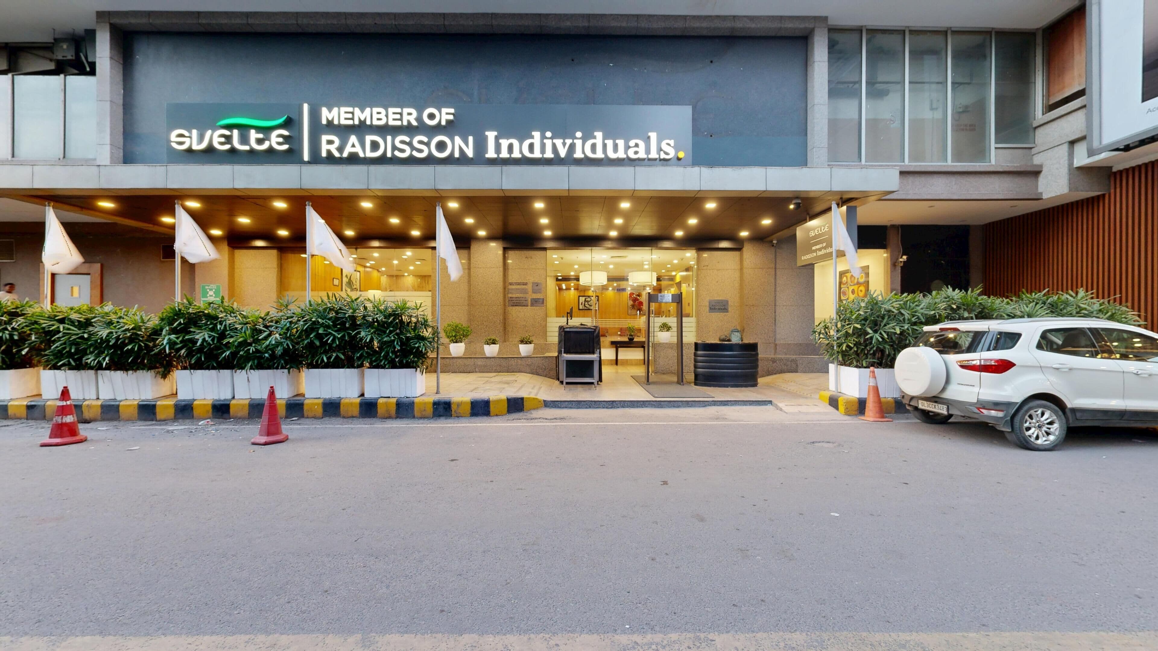 A hotel entrance with a sign indicating membership in Radisson Individuals. There are potted plants and a white car parked outside.