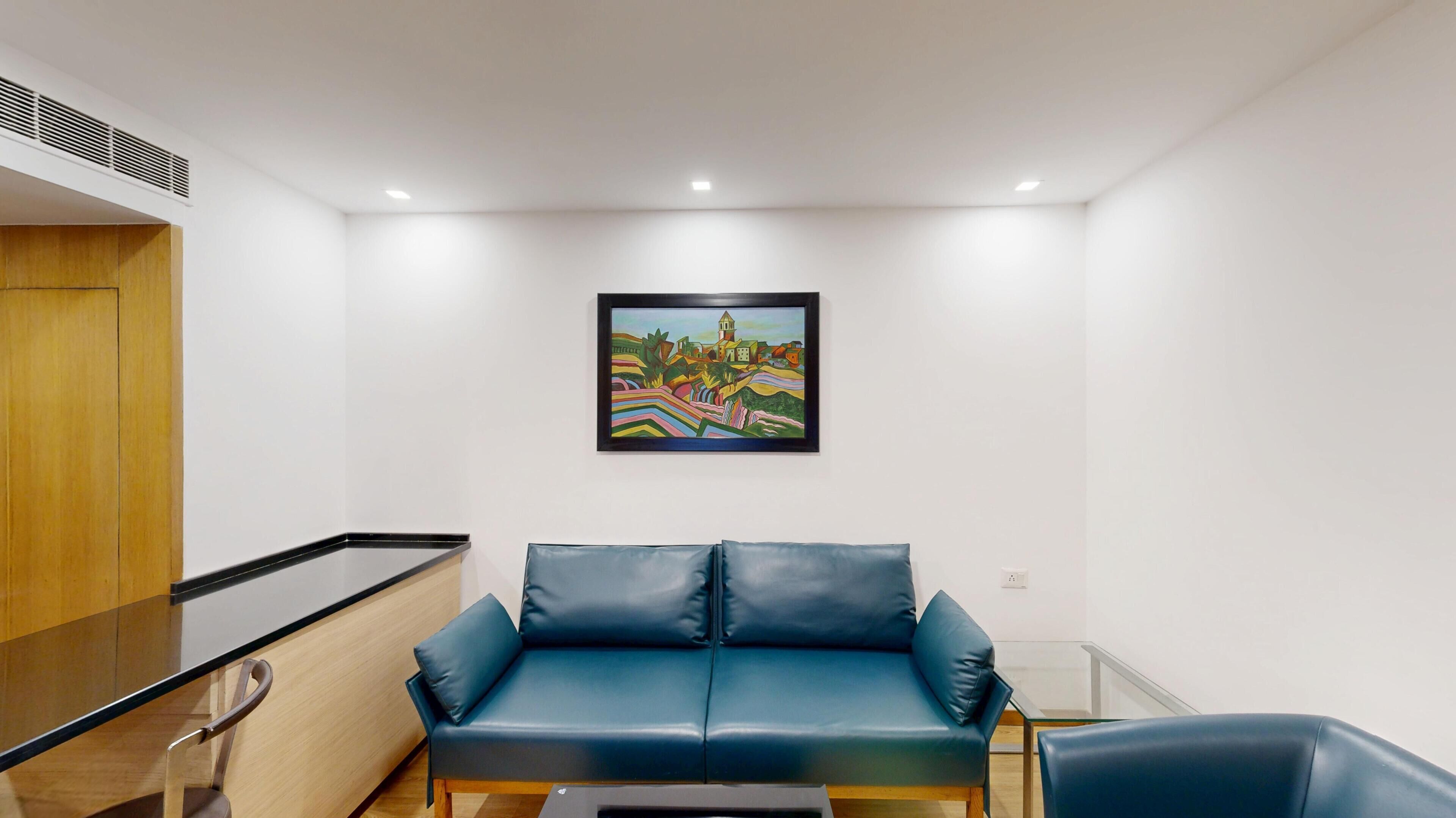 Una habitación moderna con un sofá de cuero azul, una mesa de vidrio y un cuadro colorido en la pared.