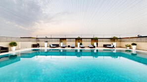 A swimming pool with lounge chairs and potted plants, surrounded by a tiled deck and a high ceiling. - Svelte Delhi, a member of Radisson Individuals (New Delhi)