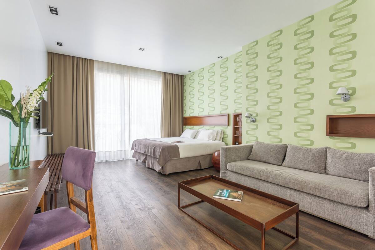 A hotel room with a bed, a sofa, a wooden coffee table, a chair, and a desk.