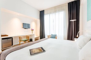 A modern hotel room with a bed, a desk, a chair, a small fridge, and a TV on the wall. - BA Jardines Palermo (Buenos Aires)