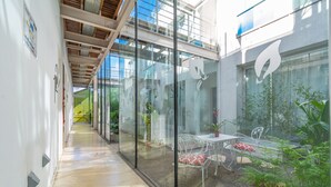 Un jardín interior moderno con paredes de vidrio, un comedor con sillas de metal y una variedad de plantas.