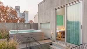 Un espacio exterior moderno con un jacuzzi, dos sillas y una mesa pequeña con bebidas.