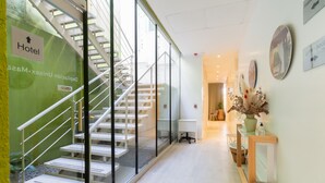 Interior de un hotel con una escalera, una recepción y una pared con indicaciones.
