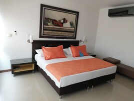 A neatly arranged bedroom with a bed, nightstands, a painting, and a wall-mounted air conditioning unit.