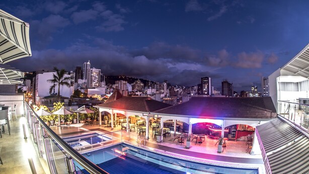 Uma área de piscina no terraço com vista para o horizonte urbano, mobiliário de exterior e um alpendre coberto.