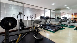 Uma academia com diversos equipamentos de exercício, incluindo esteiras, um banco de musculação e um remo.
