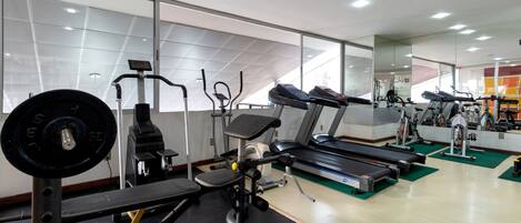 Un gimnasio con varios equipos de ejercicio, incluyendo cintas de correr, una banca de pesas y una máquina de remo.