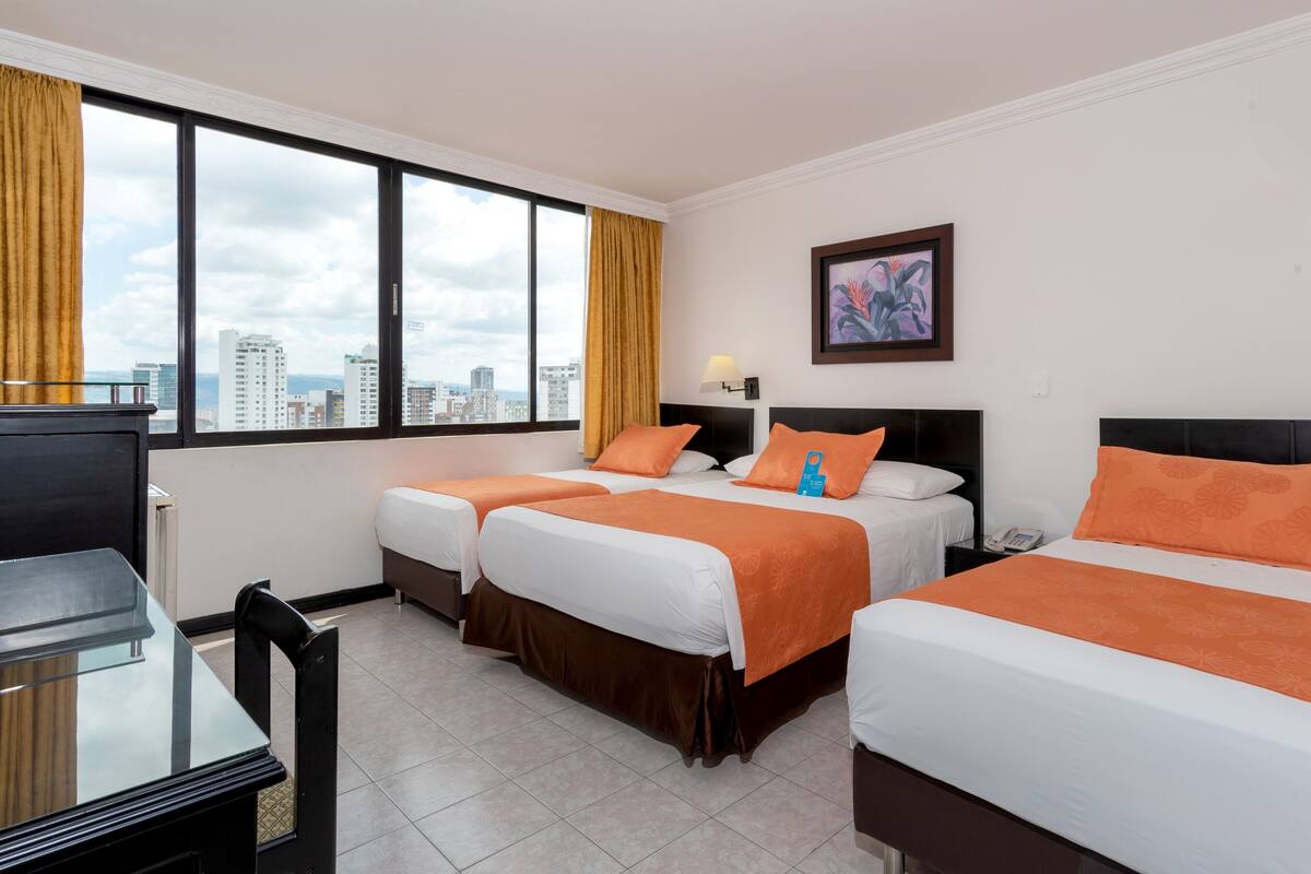 Une chambre d’hôtel avec deux lits, un bureau et une fenêtre donnant sur la ville.