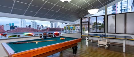A pool table in a room with large windows, a view of the cityscape, and a ceiling with a grid pattern.