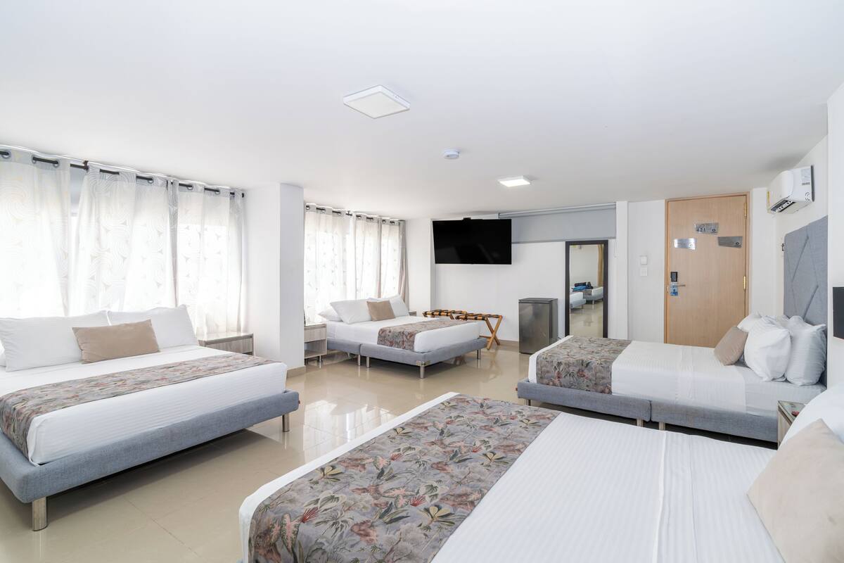A hotel room with three beds, a TV, a door, and an air conditioning unit.