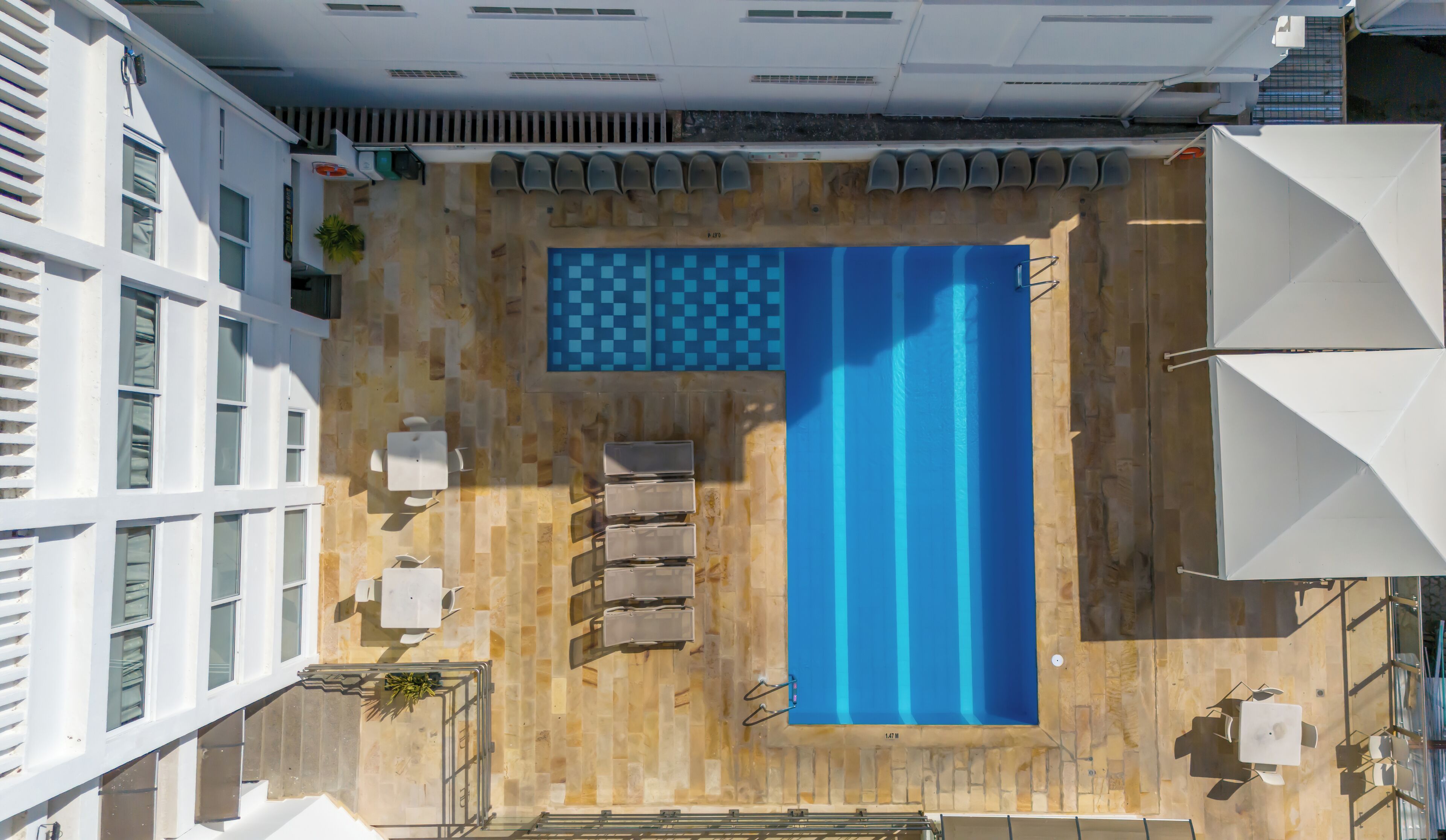 Una piscina en la azotea con un elemento decorativo de agua azul, rodeada de paredes blancas y una terraza de madera.