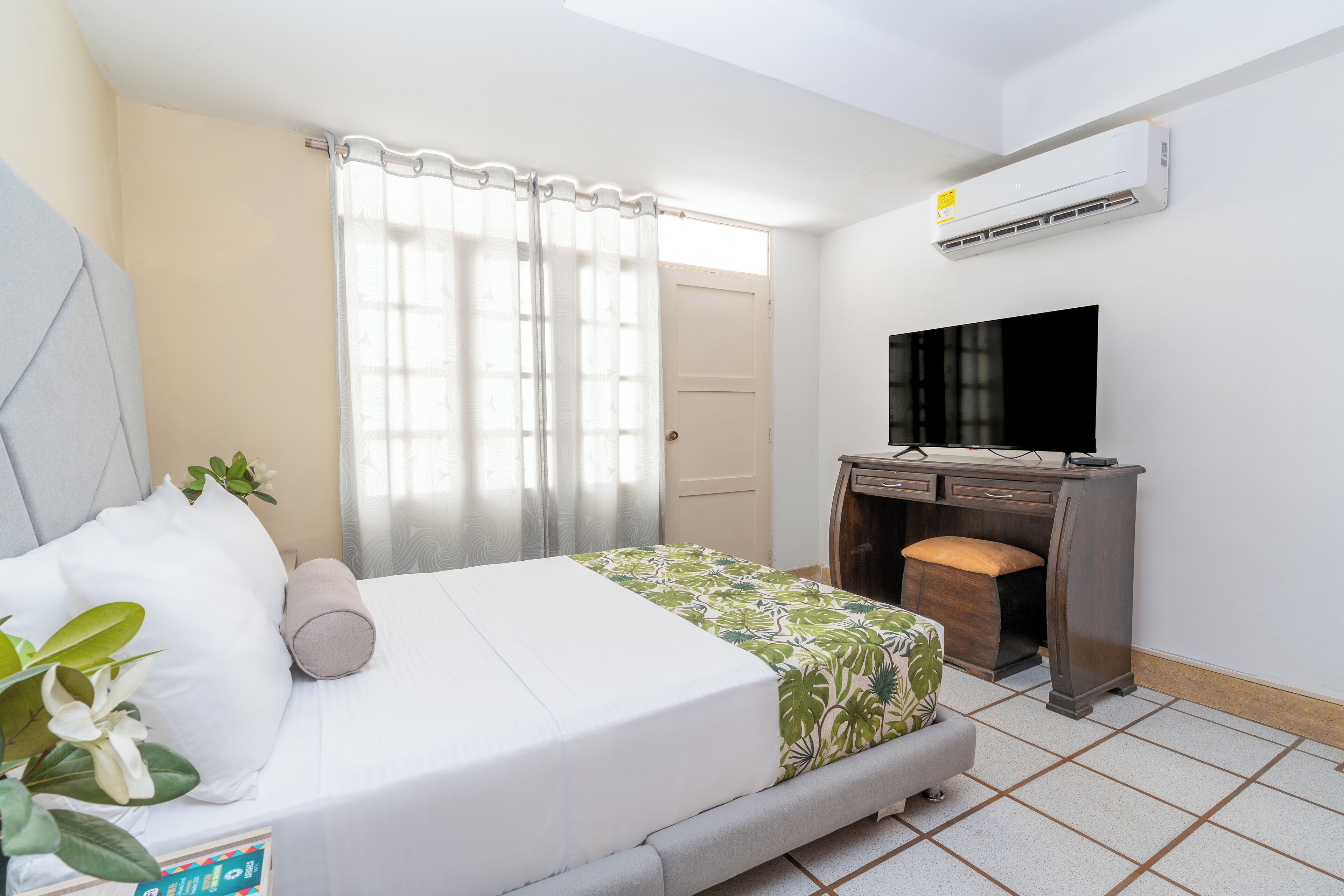 Een slaapkamer met een bed, een bureau, een televisie en een airconditioner.