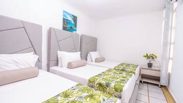 Habitación de hotel con tres camas, un escritorio pequeño y una planta en maceta.