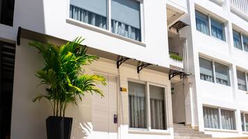 Um edifício moderno com um vaso de planta em frente, uma porta com placa de número e uma escadaria que leva a um andar superior.