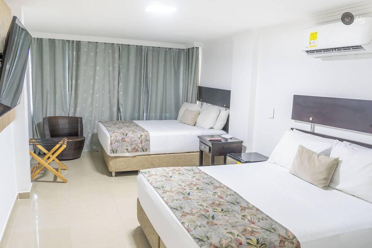 A hotel room with two beds, a desk, a chair, and an air conditioning unit.