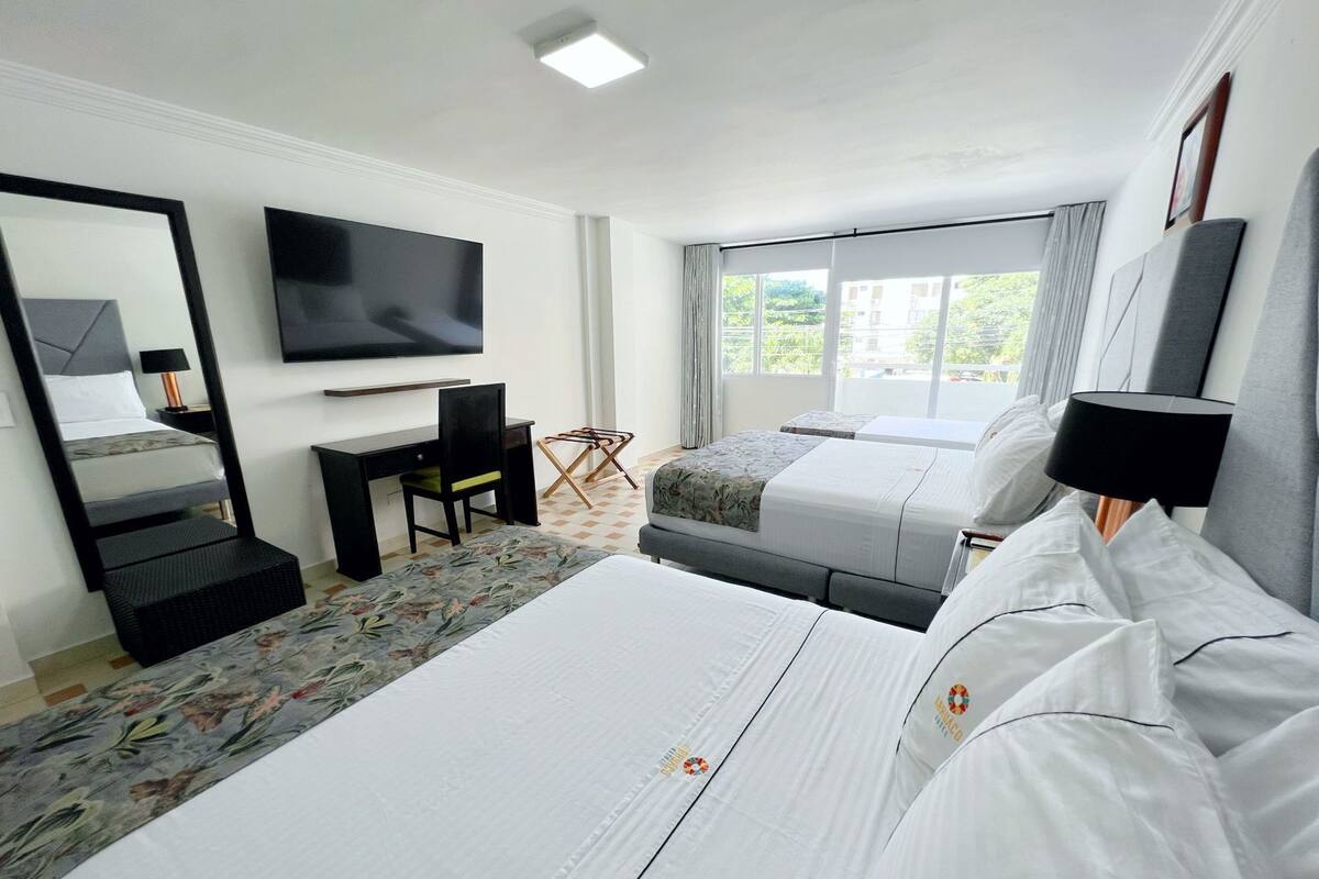 A hotel room with two beds, a desk, a chair, a television, and a window with curtains.