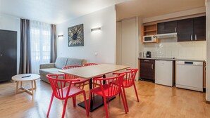 Een moderne woonkamer met een eettafel, rode stoelen, een grijze bank en een keuken met kasten en apparatuur.