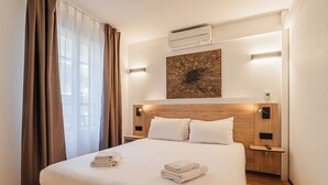 Een hotelkamer met een groot bed, een hoofdbord met ingebouwde verlichting, een airconditioningapparaat en een kunstwerk aan de wand.