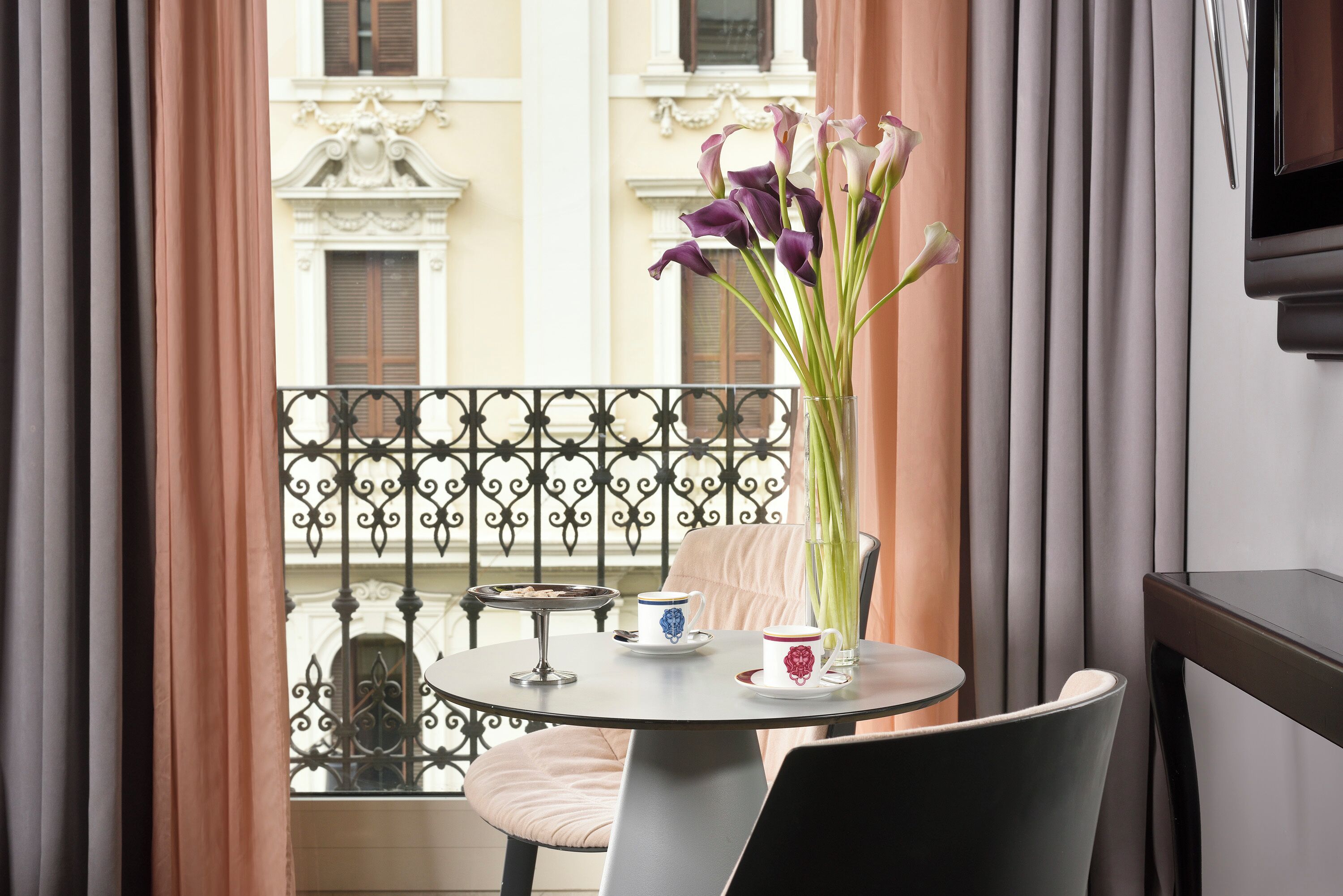 En balkon med et bord, stole, en vase med blomster og en kop og underkop.